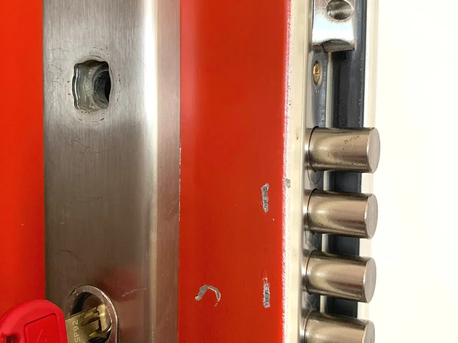 Serrure ouverte sur une porte rouge, tiges métalliques visibles